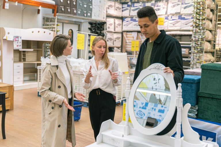 Three adults discussing a vanity set in a furniture store, engaging in shopping decisions.